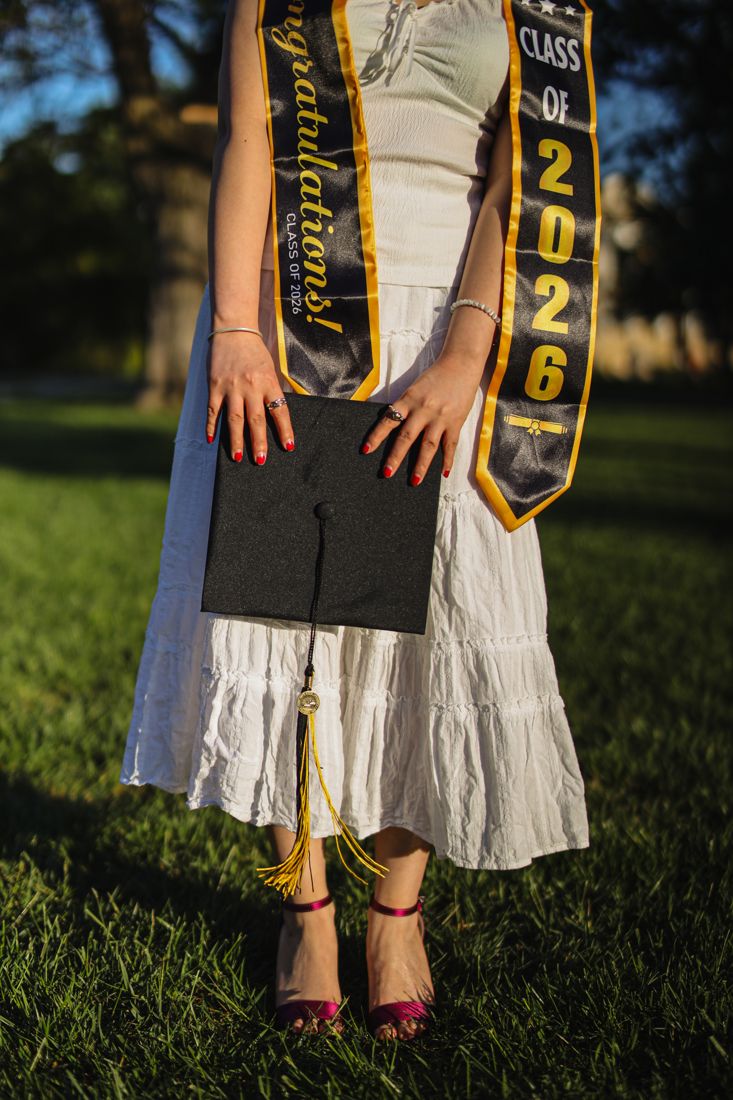 Close-up of a Class of 2026 sash and a graduation cap held against a white dress